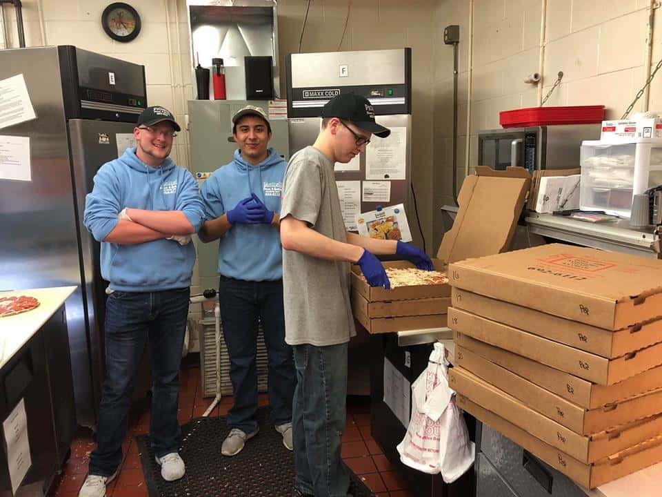 Three young employees working in a kitchen placing pizzas in boxes