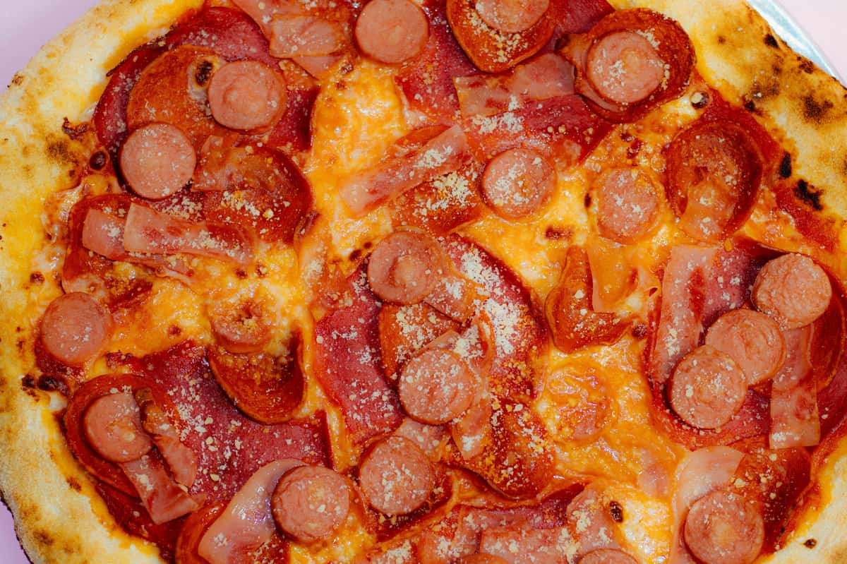 Top view of a loaded meat lovers pizza with sausage slices, ham, pepperoni, and a dusting of parmesan on melted cheese.