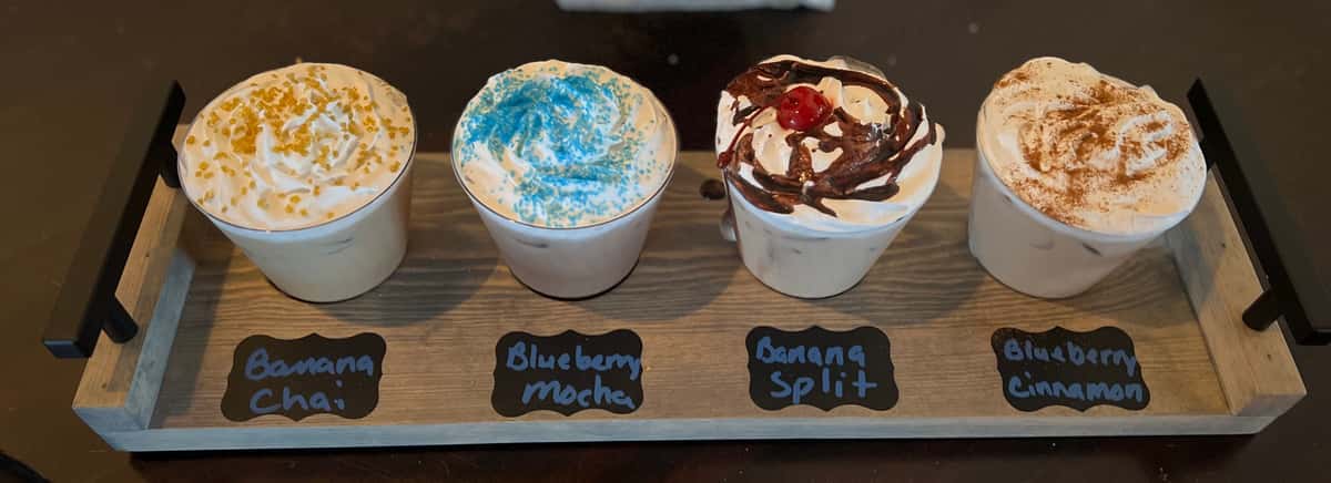 A tray of four specialty iced drinks topped with whipped cream and various toppings at AJ's Riverside.