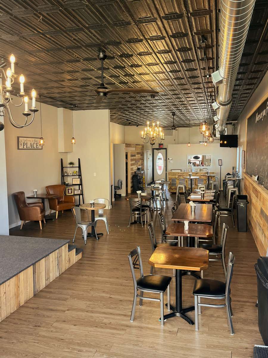 AJ's Riverside restaurant interior with dining tables, stage area, wood floors, and decorative tin ceiling.