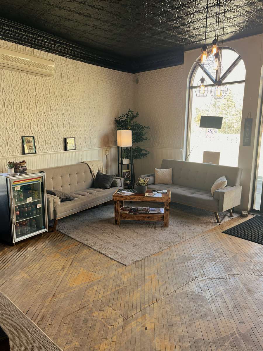 Cozy waiting area at AJ's Riverside featuring grey couches, patterned walls, wood block floor, and arched window.