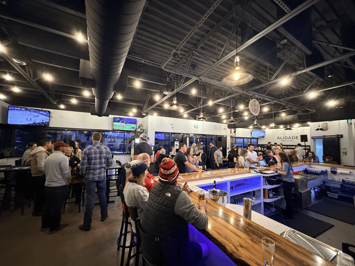 Lively crowd enjoying craft beer and conversation inside Alidade Brewing's modern taproom with a spacious bar and social atmosphere.