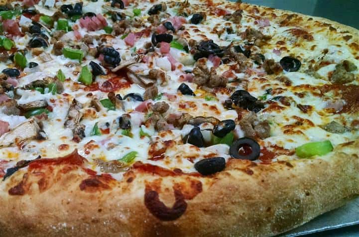 Pizza with multiple toppings including peppers, black olives, ham, and more