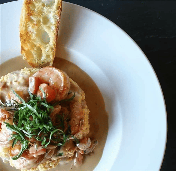 Risotto topped with a creamy sauce, shrimp, basil shreds, and a slice of toasted bread on the side.