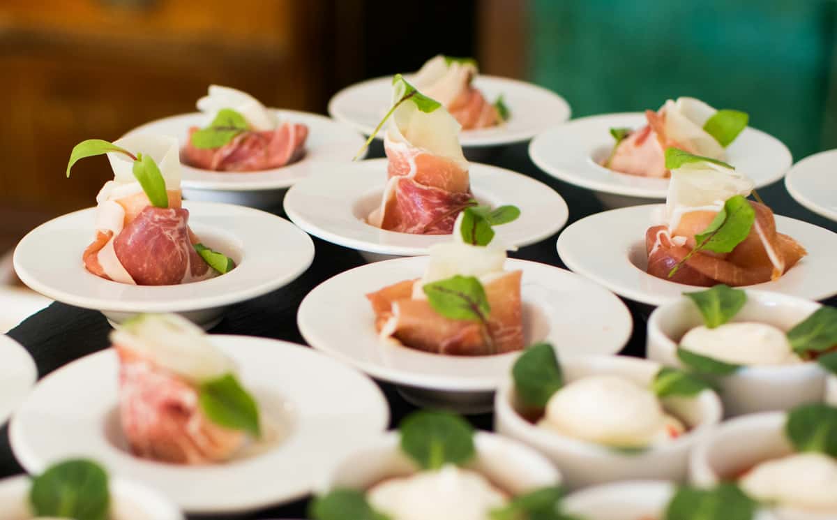 Elegant bite-sized prosciutto and cheese appetizers garnished with microgreens in white dishes