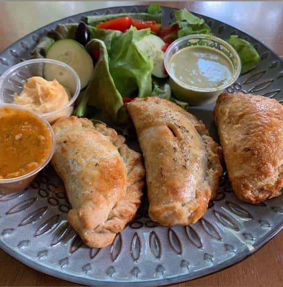 empanadas on a plate with a side salad and dipping sauces