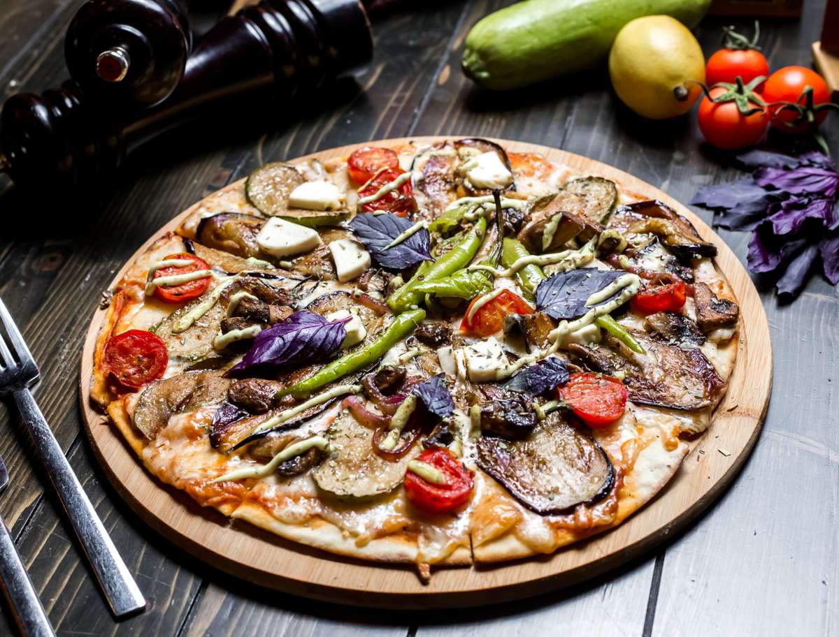 Cheezy Pizza's rustic vegetarian pizza brimming with colorful vegetables and cheese sits on a wooden board.