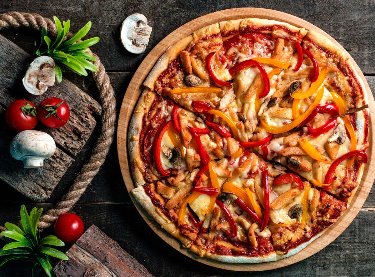 Cheezy Pizza's veggie pizza with bell peppers and mushrooms sits on a wooden board.