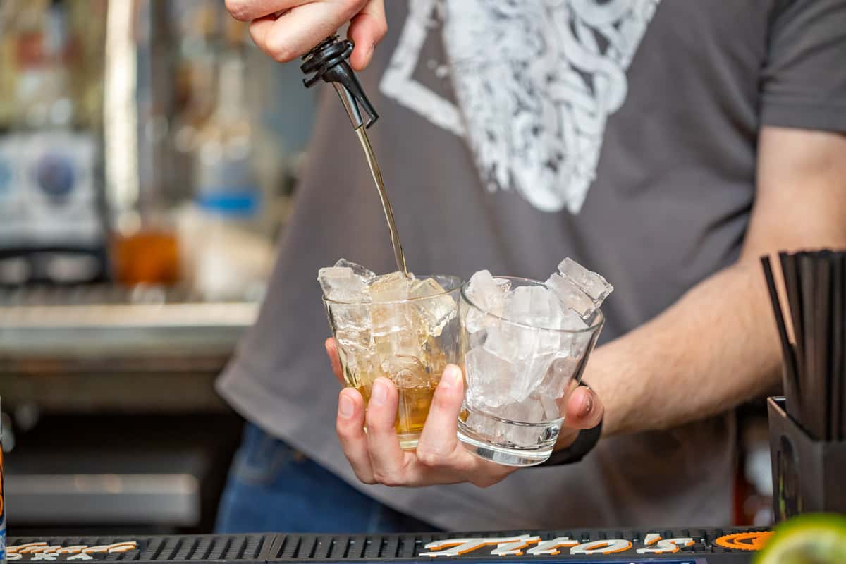 Bartender pouring liquor over ice into rocks glasses, crafting a premium cocktail at Pourhouse Bar & Grill in Loveland. Image 6: