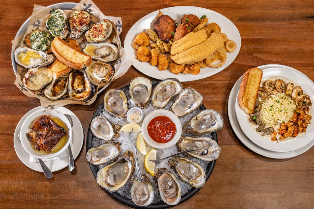 Seafood feast with raw oysters on ice, chargrilled oysters, fried seafood platter, and pasta with shrimp and garlic bread.