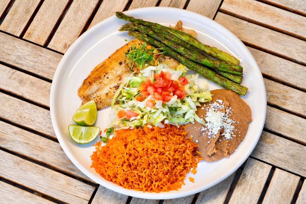 Grilled white fish plate with roasted asparagus, Mexican rice, refried beans, and fresh lime wedges