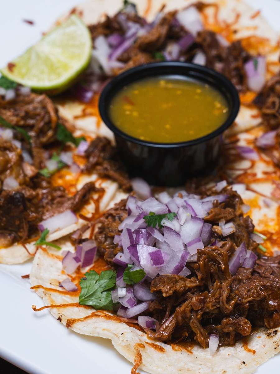 Slow-cooked beef birria tacos topped with diced red onions and cilantro, served with green salsa and fresh lime wedge