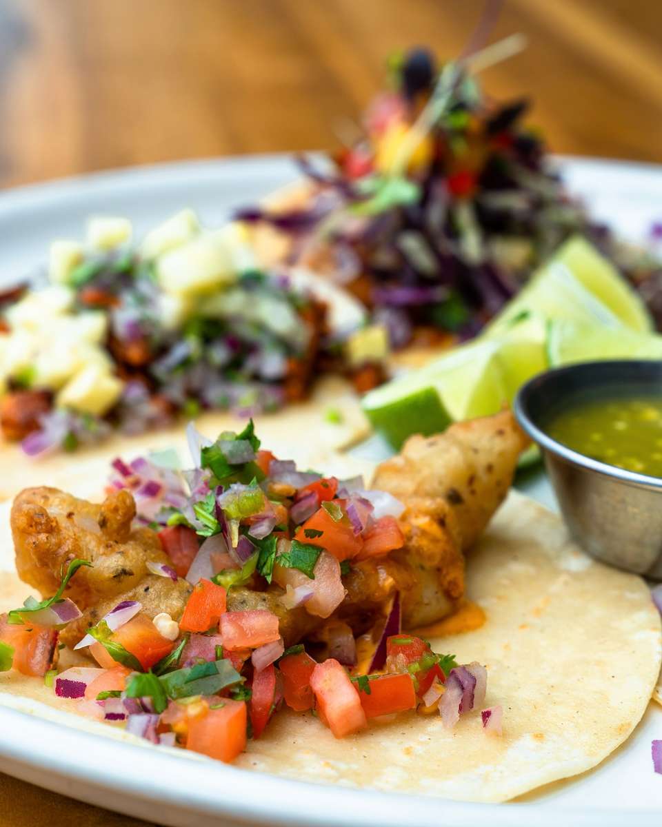 Crispy fish taco topped with fresh pico de gallo and cilantro, served with green salsa, lime wedges, and assorted Mexican street tacos