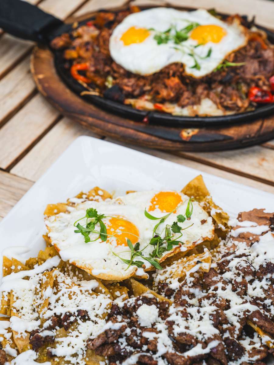 Loaded carne asada chilaquiles topped with fried eggs, queso fresco, and crema served with sizzling skillet brunch plate