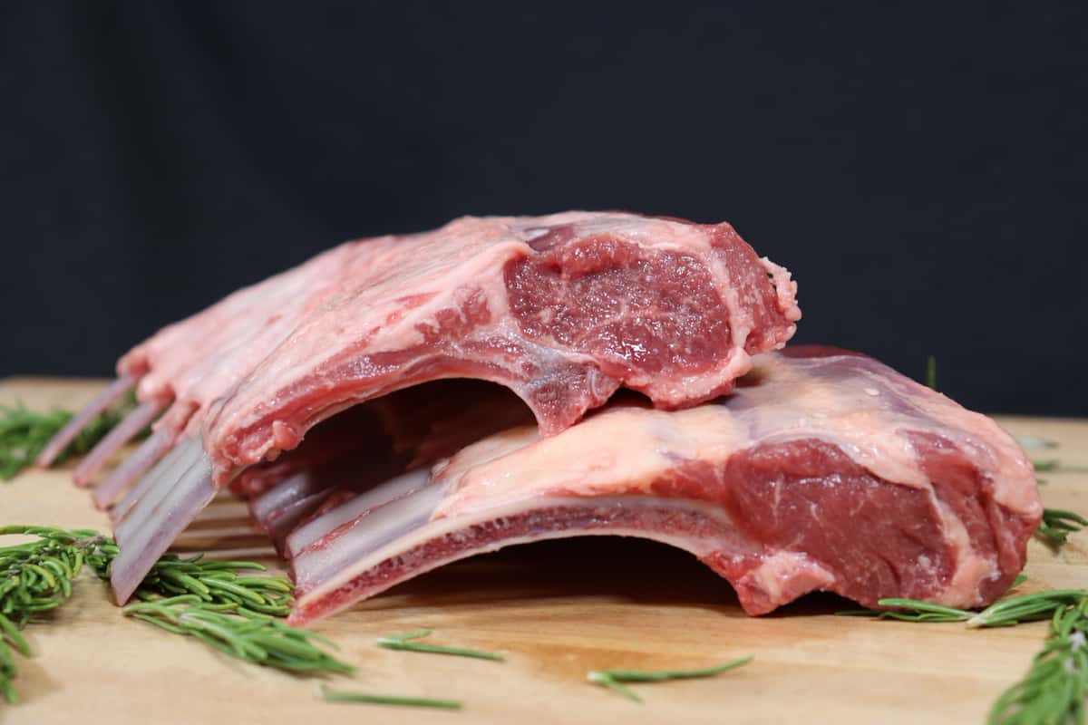Fresh raw beef ribs arranged on a wooden cutting board with rosemary.