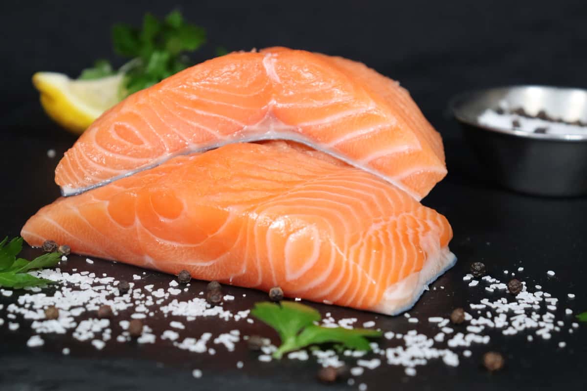 Fresh raw salmon fillets displayed on a bed of ice with coarse salt and herbs.