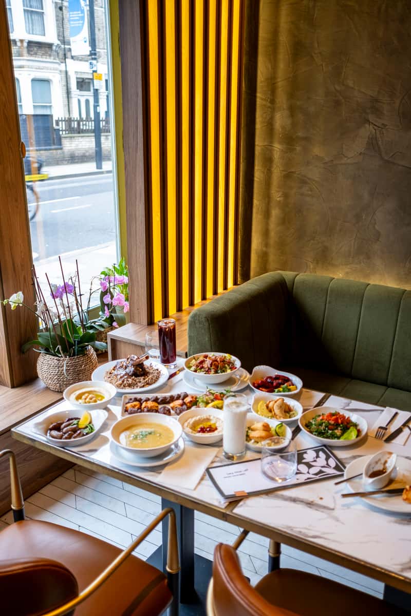 Elegant Mediterranean dining setup with mezze platters, grilled dishes, and ayran drinks beside a cozy booth seating area