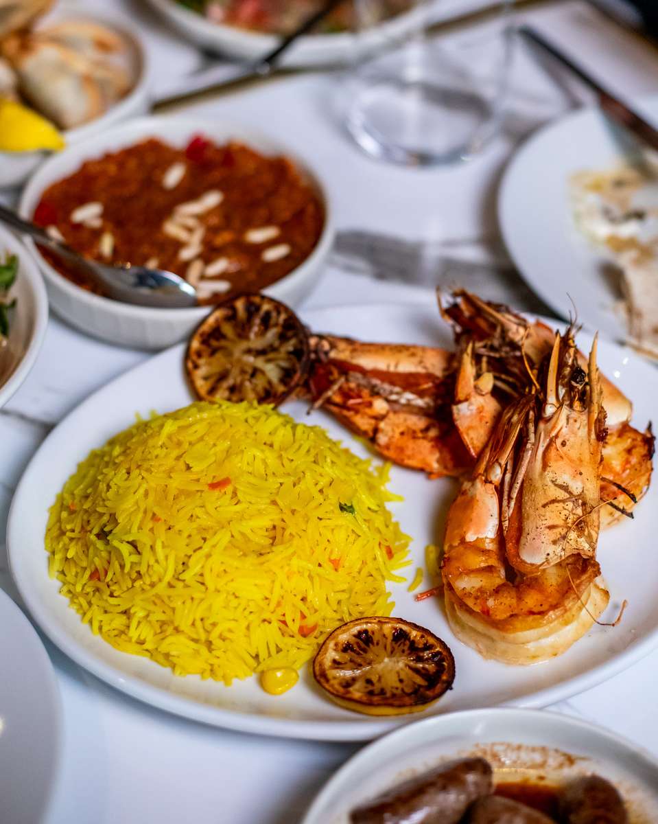 Grilled jumbo shrimp served with saffron rice, charred lemon, and Mediterranean mezze on an elegant restaurant table