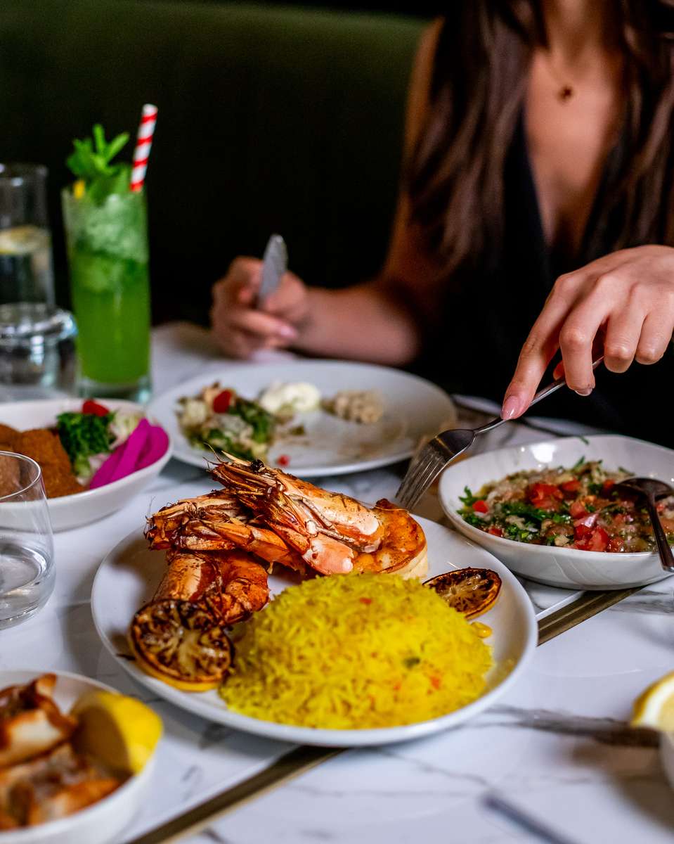Guest enjoying grilled jumbo shrimp served with saffron rice, charred lemon, and fresh Mediterranean mezze at a modern restaurant