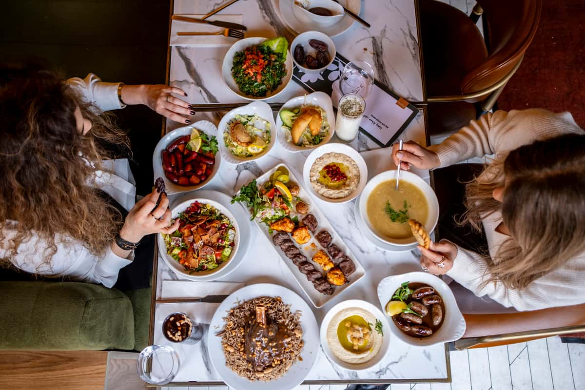 Overhead view of friends sharing a Mediterranean feast with grilled kebabs, hummus, lentil soup, fattoush salad, and traditional mezze dishes
