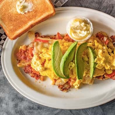 homefries topped with cheese, egg, and avocado with toast on the side