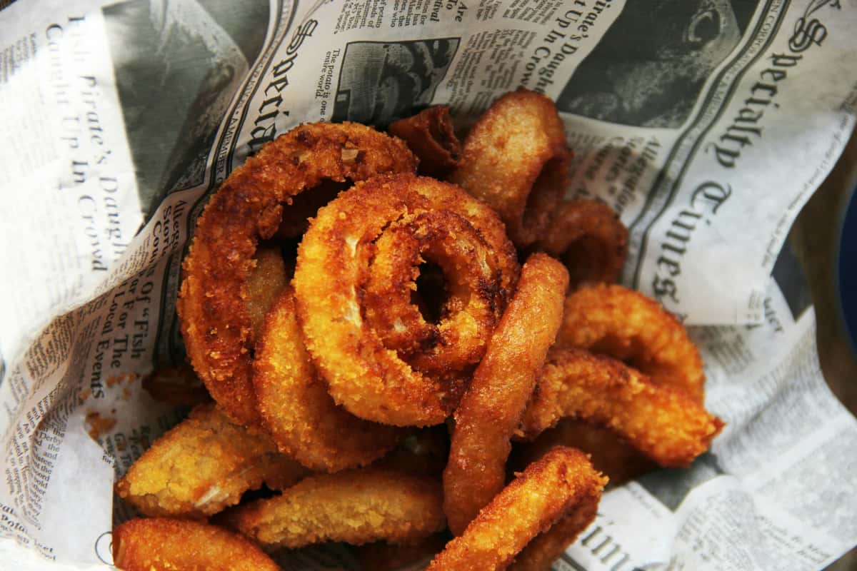 A basket filled with crispy, golden onion rings wrapped in newspaper.