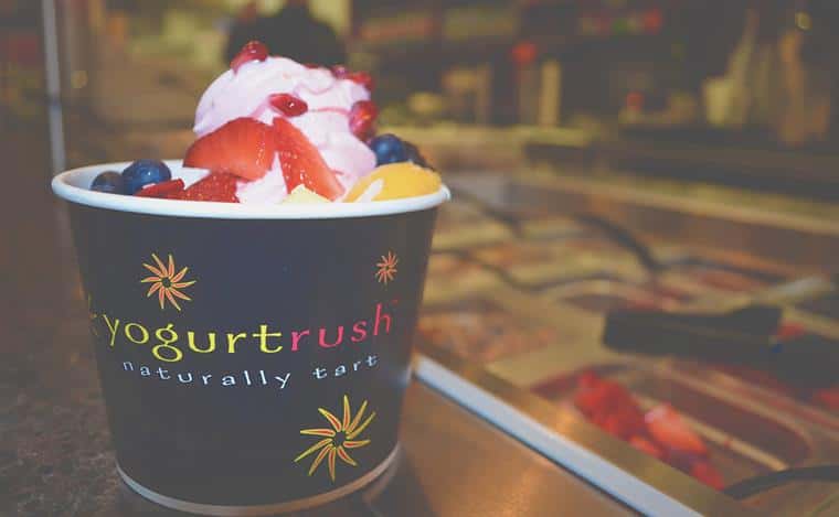 Cup of Yogurt Rush naturally tart yogurt with strawberries and blueberries next to toppings containers.