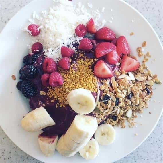 dish with granola, almonds, bananas, strawberries, raspberries, blackberries, shredded coconut.