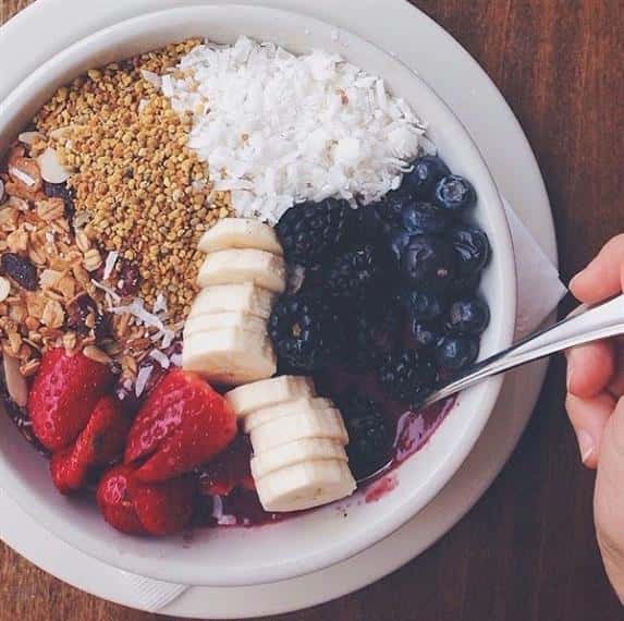 Bowl of granola, cereal, coconut shreds, strawberries, bananas, blackberries, blueberries.