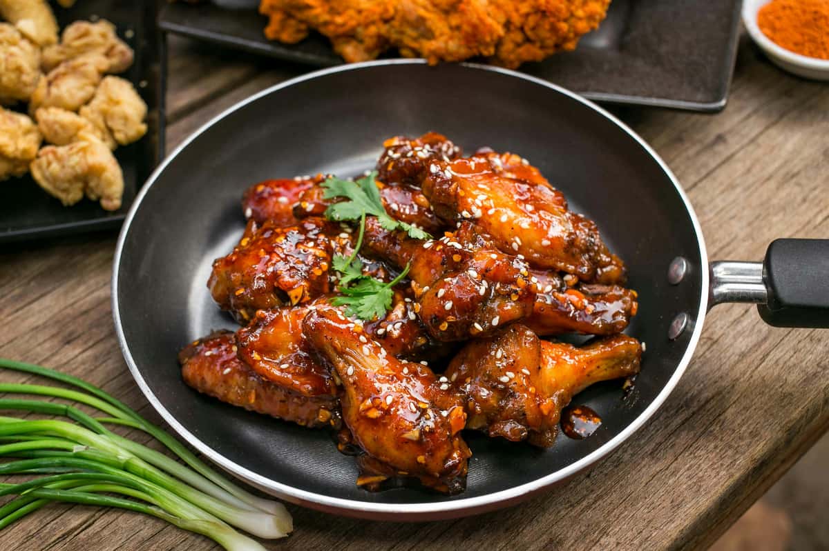 glazed chicken wings in a skillet topped with sesame seeds and herbs, served with crispy fried chicken sides
