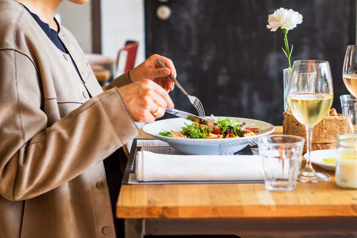 A woman sitting at a table using a fork and knife to eat a meal