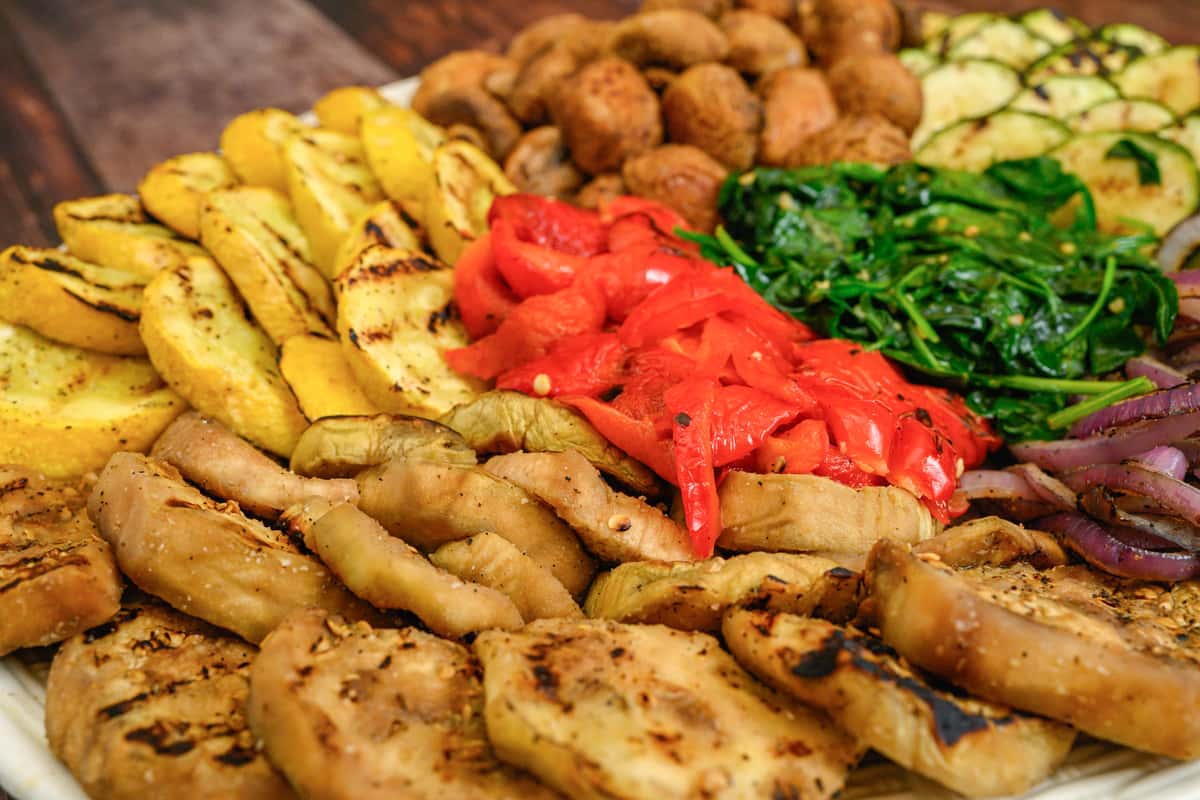 Colorful grilled vegetable platter with squash, eggplant, bell peppers, spinach, onions, zucchini, and falafel arranged in sections.