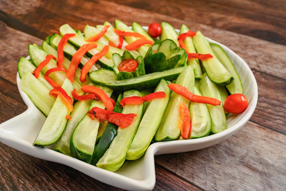 Sliced cucumbers arranged on a fish-shaped platter, garnished with red bell pepper strips and cherry tomatoes.