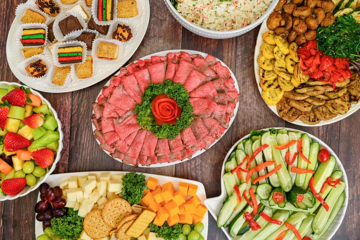 Assorted party platters with roast beef, cheese and crackers, cucumber salad, grilled vegetables, fruit, pasta salad, and desserts.