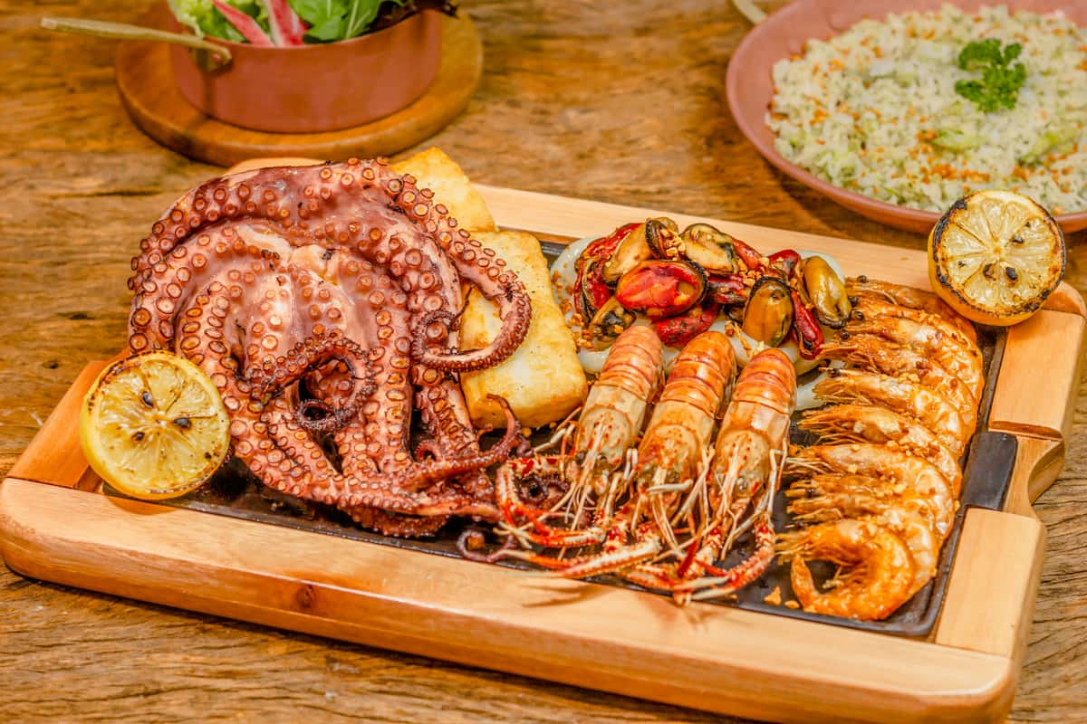Assorted grilled seafood including octopus, prawns, mussels, and grilled lemons served on a wooden tray, offering a vibrant coastal-inspired seafood feast.