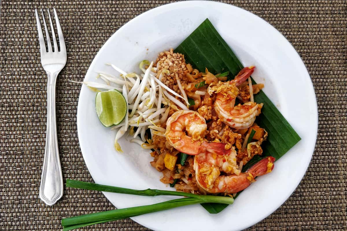 Pad Thai with shrimp served on a white plate with bean sprouts, lime, peanuts, and banana leaf garnish.