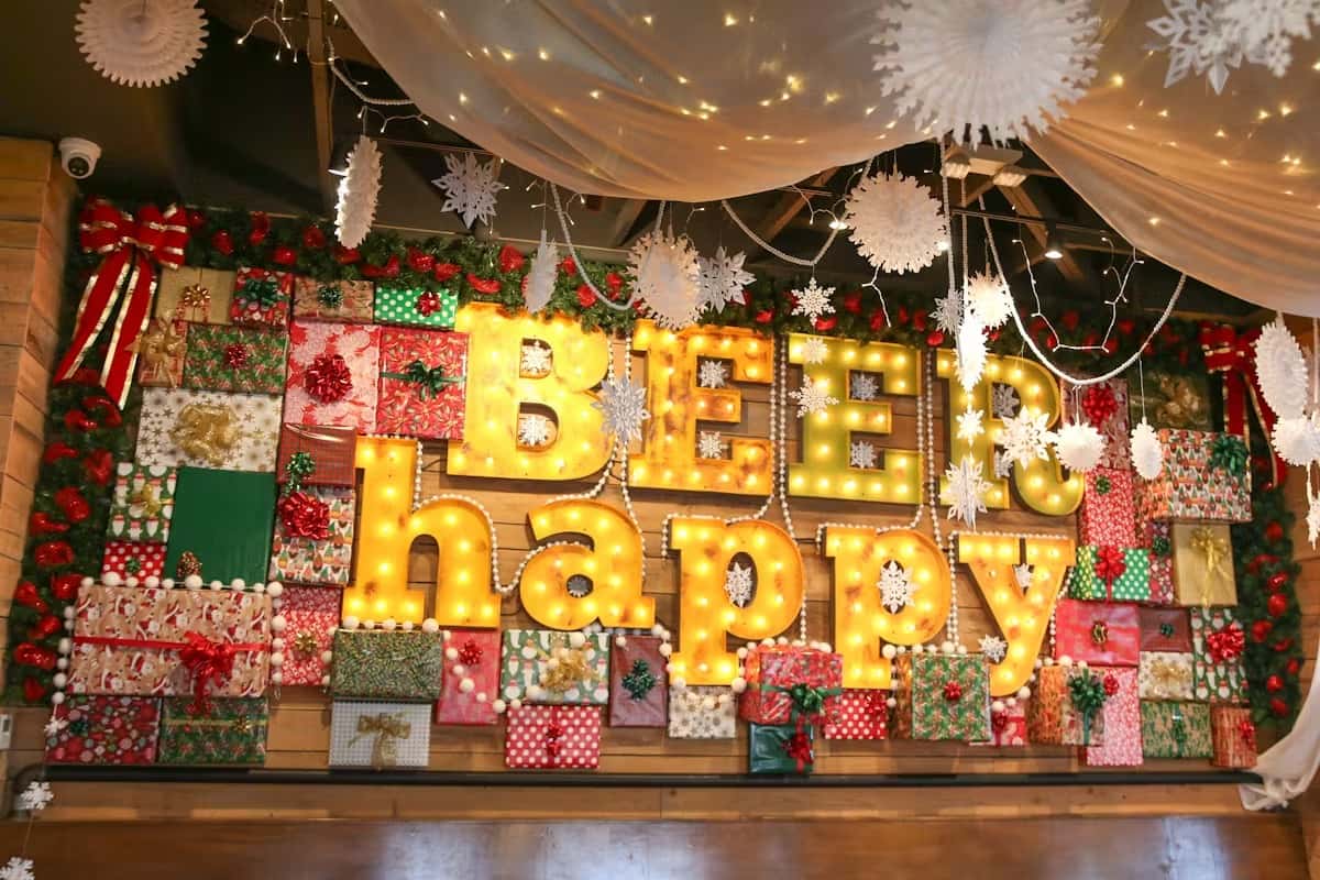 Light-up "Beer Happy" sign on a wall decorated with holiday gift boxes, snowflakes, and festive garland.
