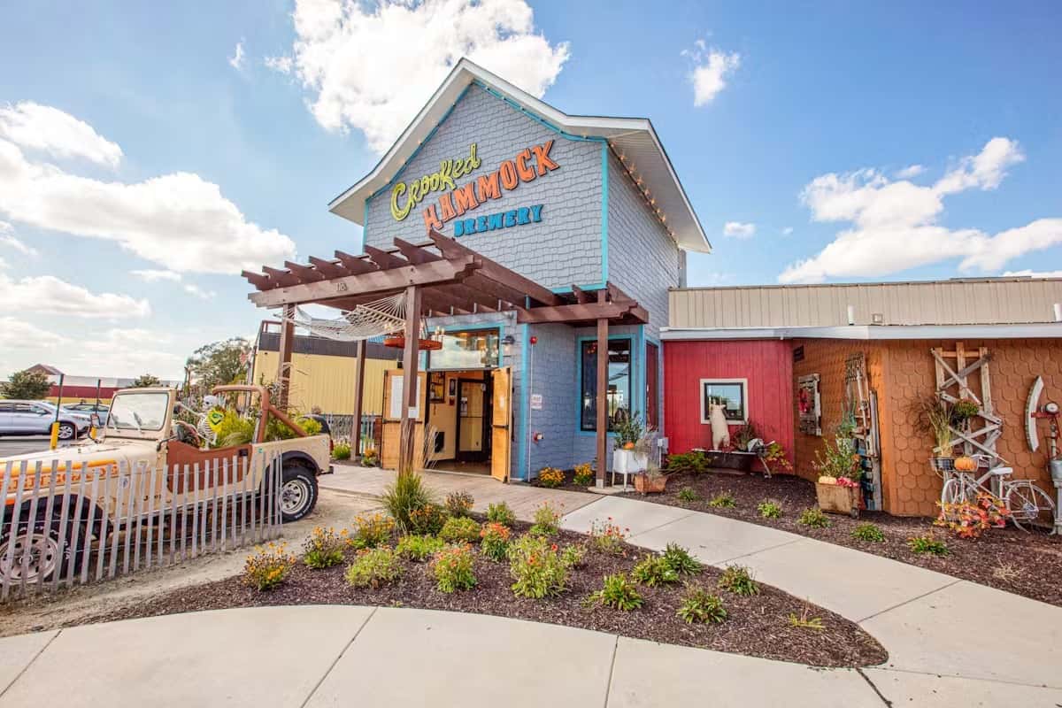 Exterior of Crooked Hammock Brewery with a colorful entrance, decorative garden, and a vintage Jeep parked nearby.