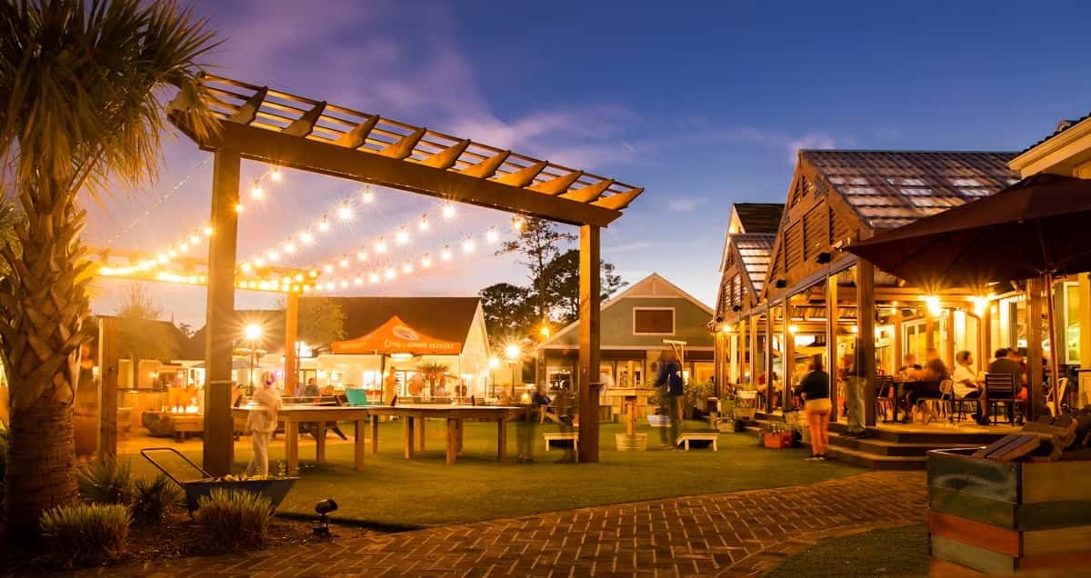 String lights and wooden pergolas light up the outdoor seating area at Crooked Hammock Brewery during a warm evening.