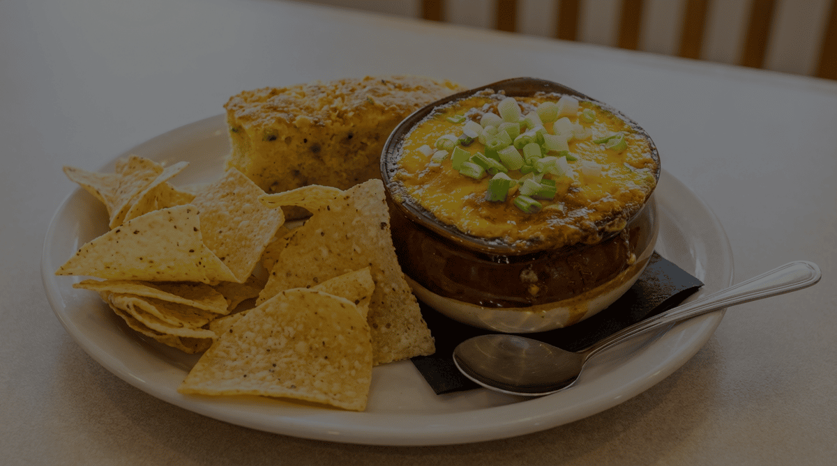Bowl of chili topped with cheese and green onions, served with tortilla chips and cornbread.