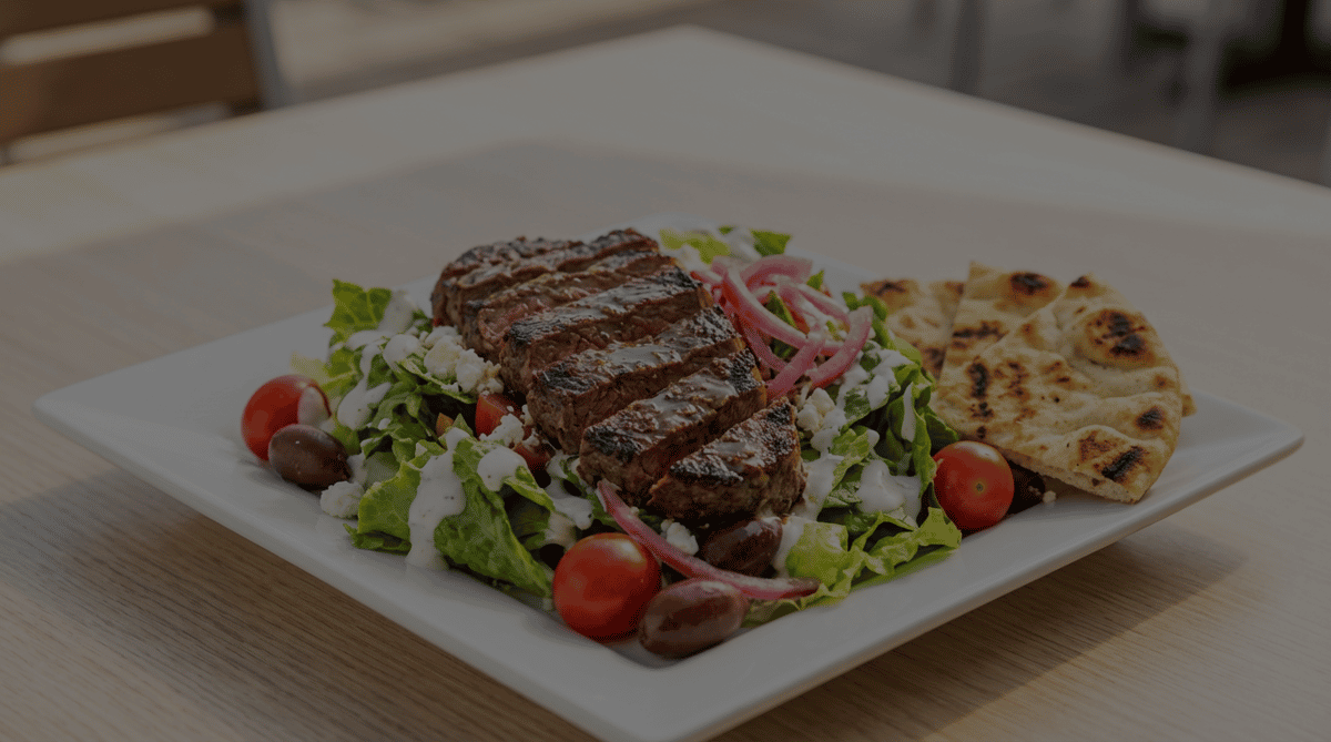 Steak salad with mixed greens, olives, feta, cherry tomatoes, pickled onions, and white dressing, served with pita bread.