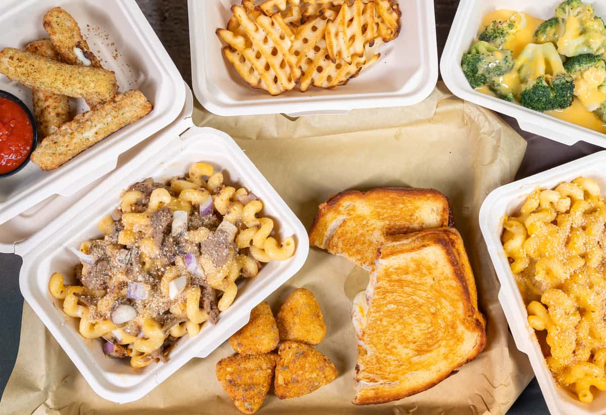 Assorted takeout containers with mac and cheese, waffle fries, and a grilled sandwich