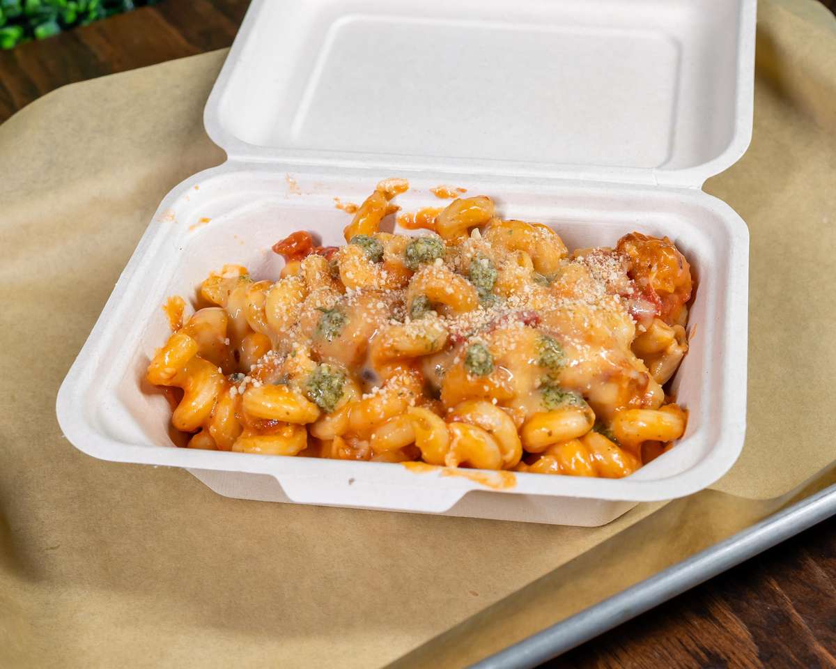 Mac and cheese topped with crispy bacon bits and fresh herbs in a to-go container