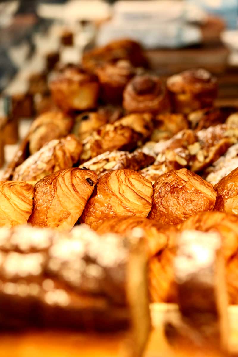 Assorted golden pastries and croissants displayed in a bakery with warm lighting
