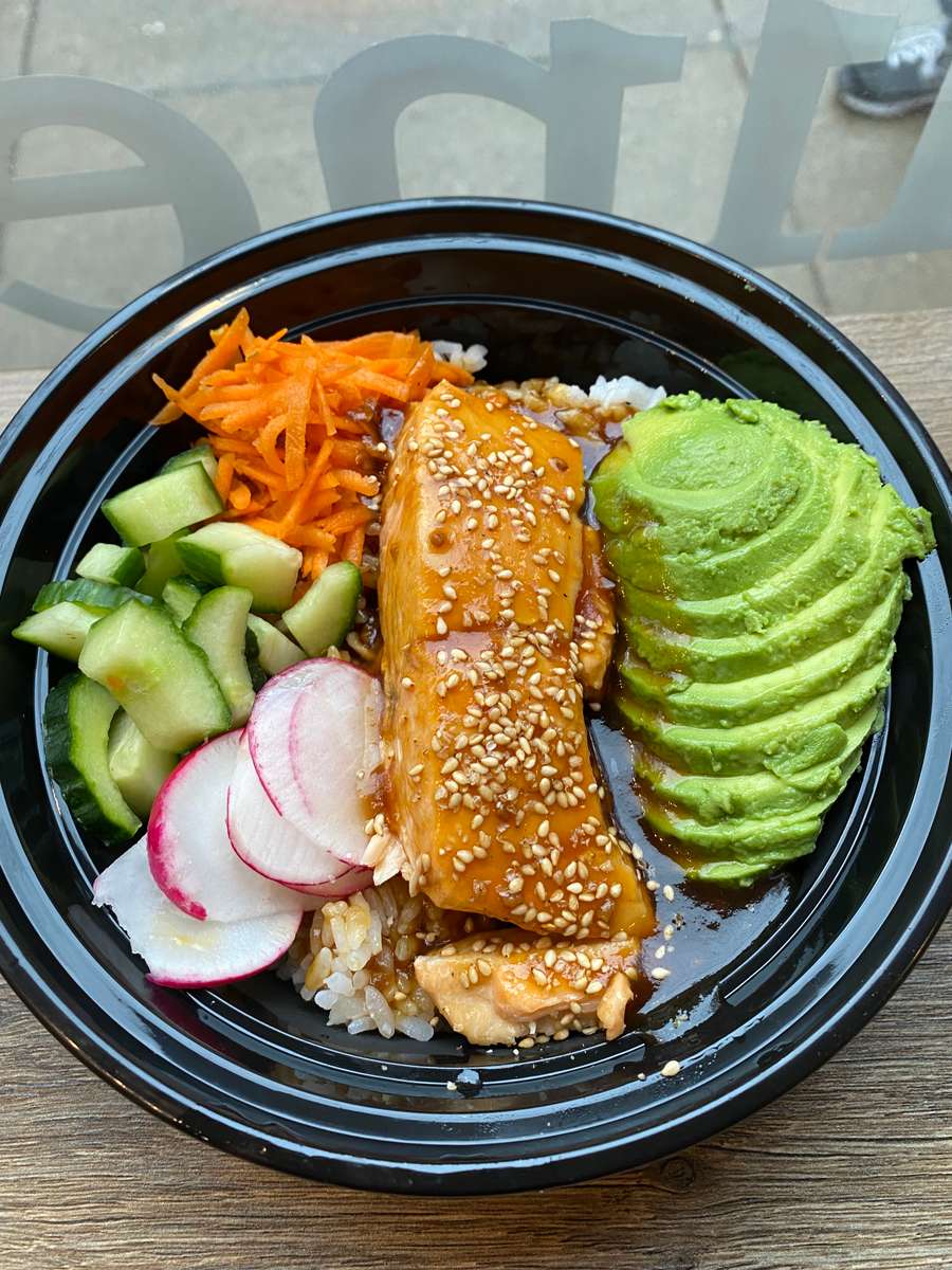 Close up picture of an Asian style salmon bowl with teriyaki sauce, avocado, cucumber, radishes, carrots, and sesame seeds on a bed of rice