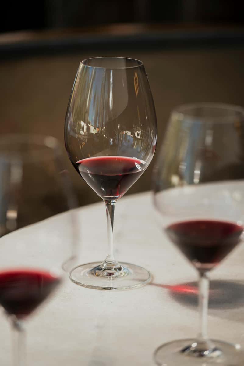 Partially filled wine glass with red wine on a white table, surrounded by other similar glasses in soft focus.
