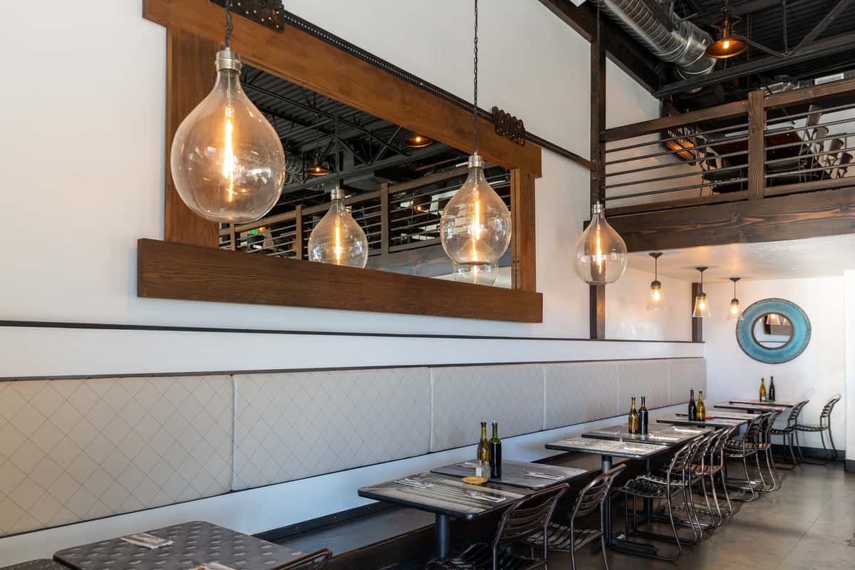 Modern Italian bistro interior with industrial lighting, wood and metal accents, cozy booth seating, and a mezzanine dining area.