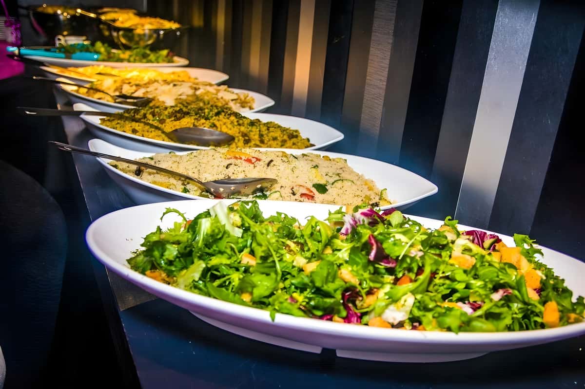 Buffet table with large platters of fresh salad and prepared dishes.