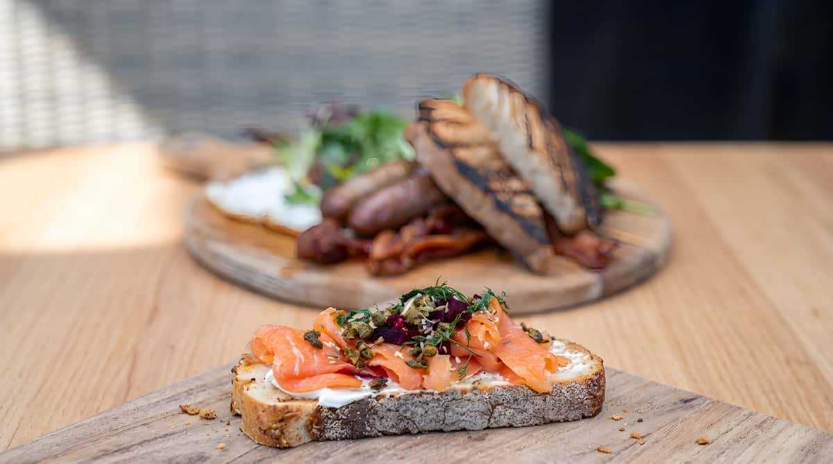 Smoked salmon toast topped with greens and herbs on a wooden board.