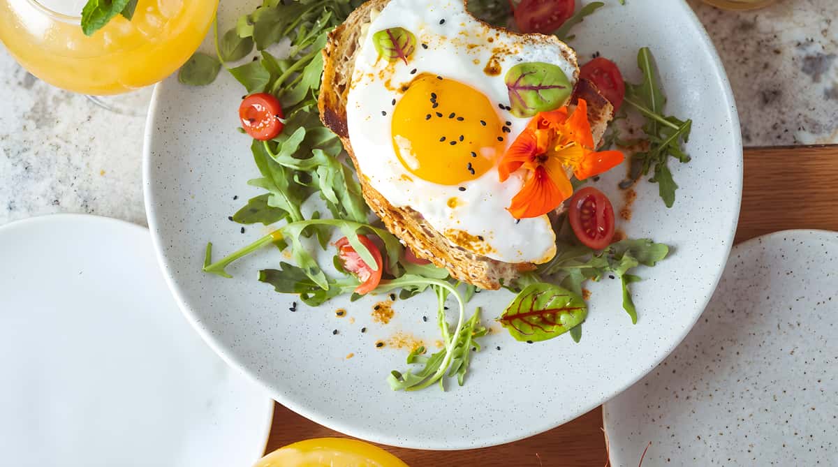 Toast topped with a fried egg, arugula, and sliced cherry tomatoes.